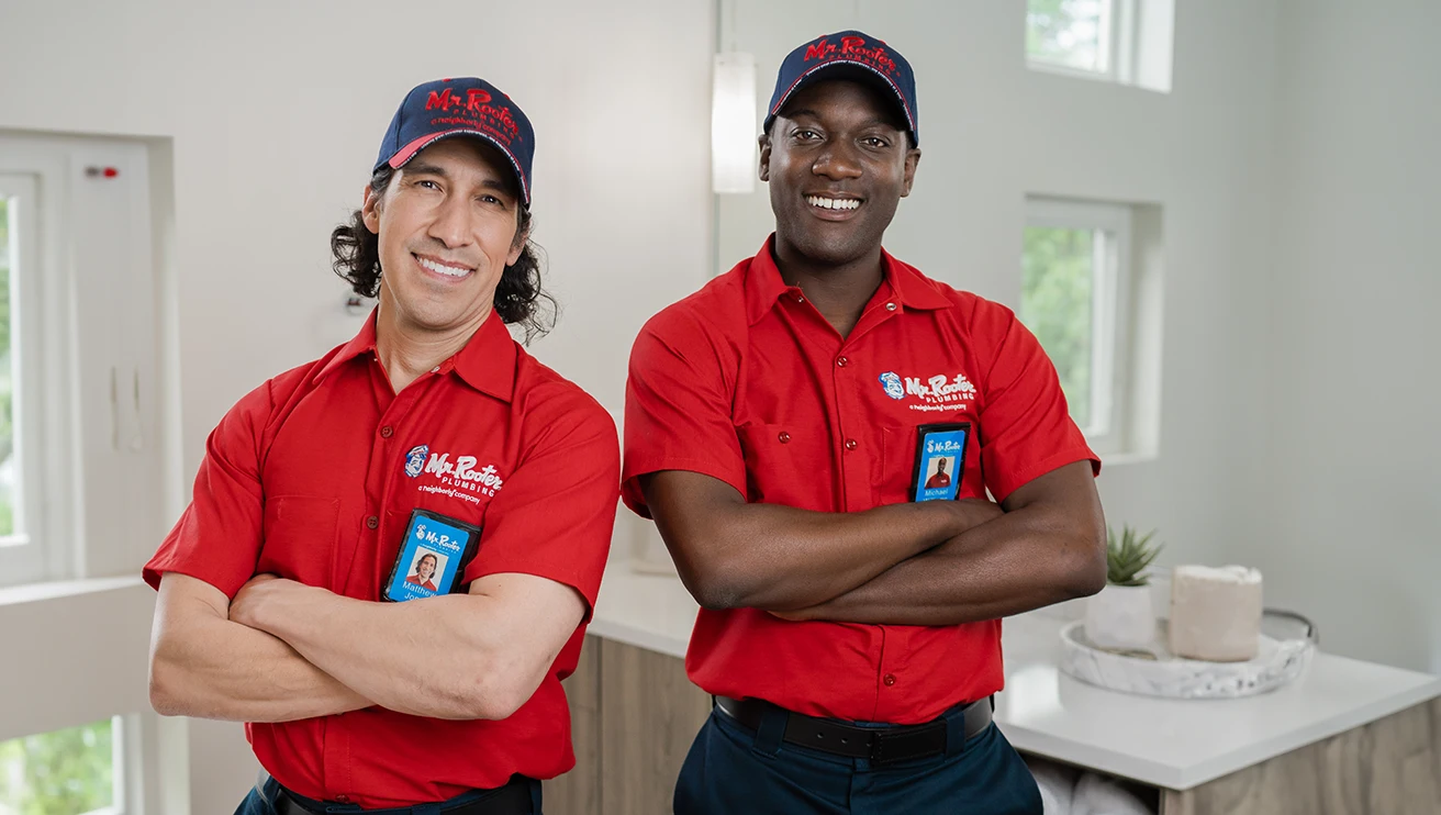 Two Mr. Rooter technicians standing in a bathroom with their arms crossed.