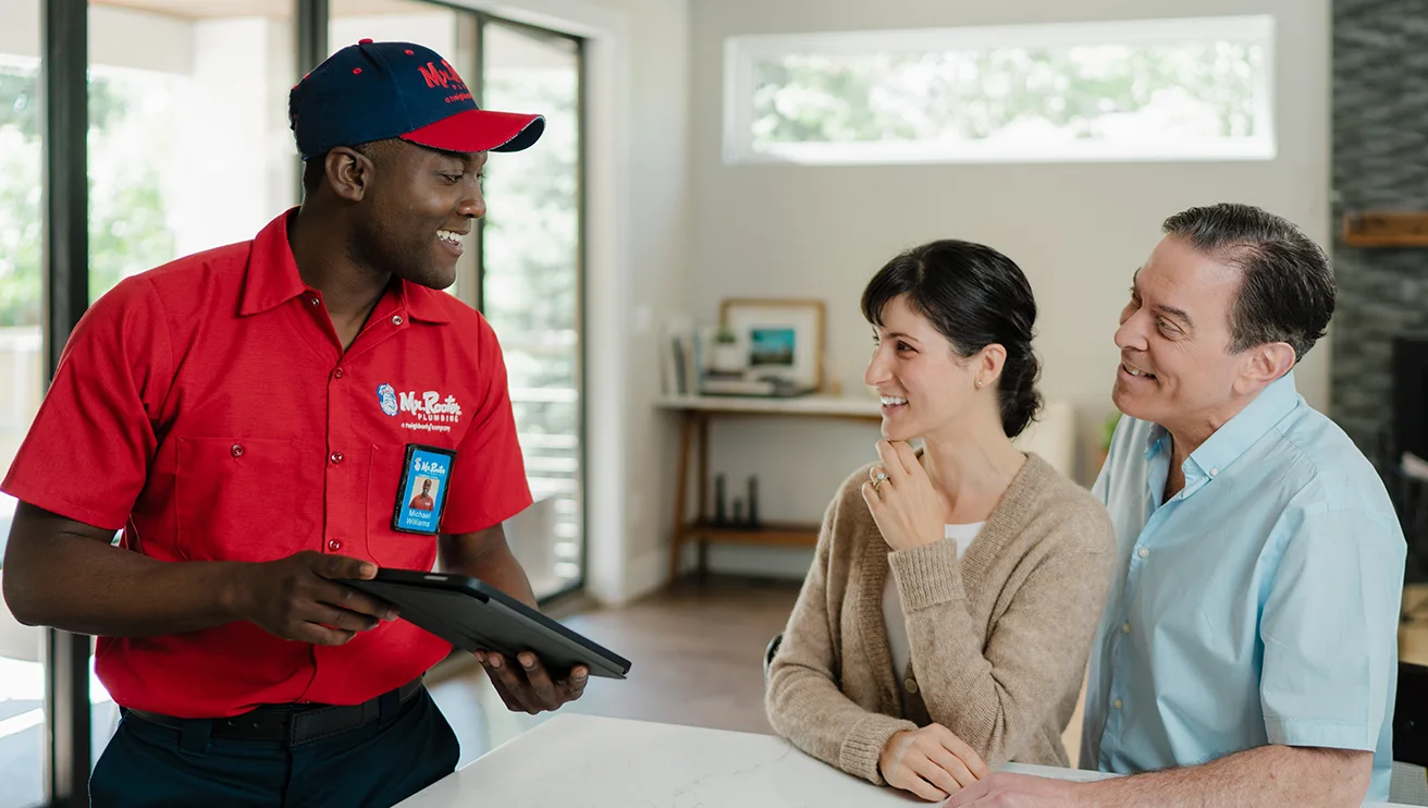 Mr. Rooter technician going over service options with two customers on a tablet.