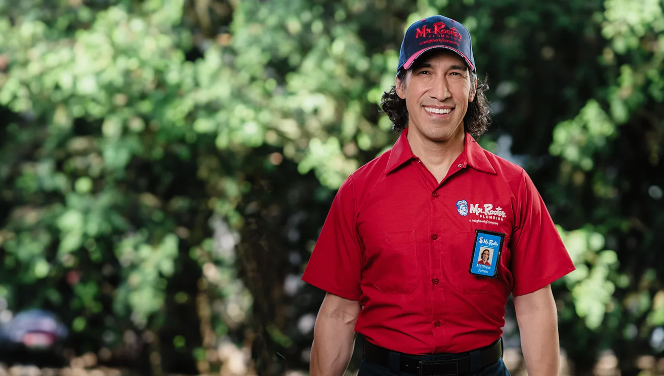 Mr. Rooter technician standing outside in front of a wall of greenery.