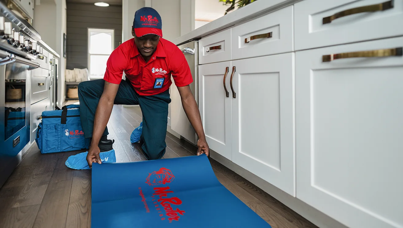 Mr. Rooter technician placing a mat in front of a customer's kitchen cabinets.