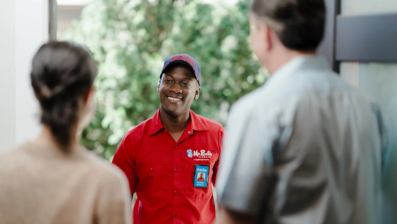 Two customers greeting a Mr. Rooter technician at their front door.