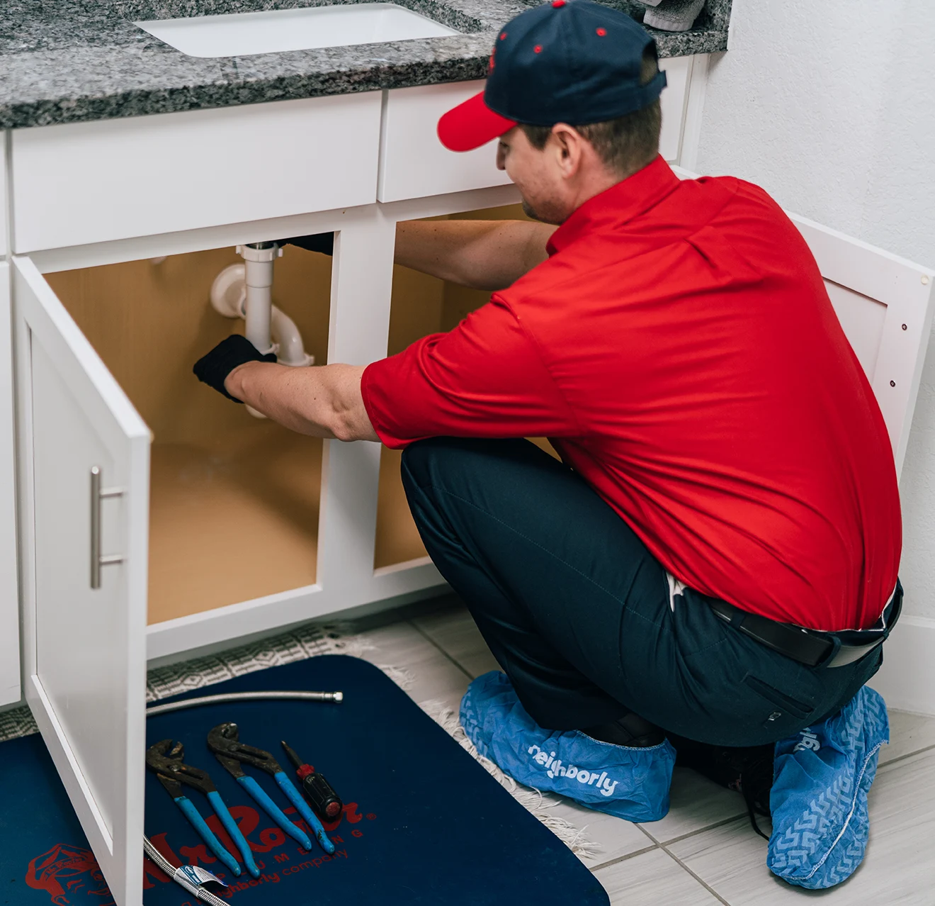 Mr. Rooter technician working on cleaning a drain underneath a sink vanity.