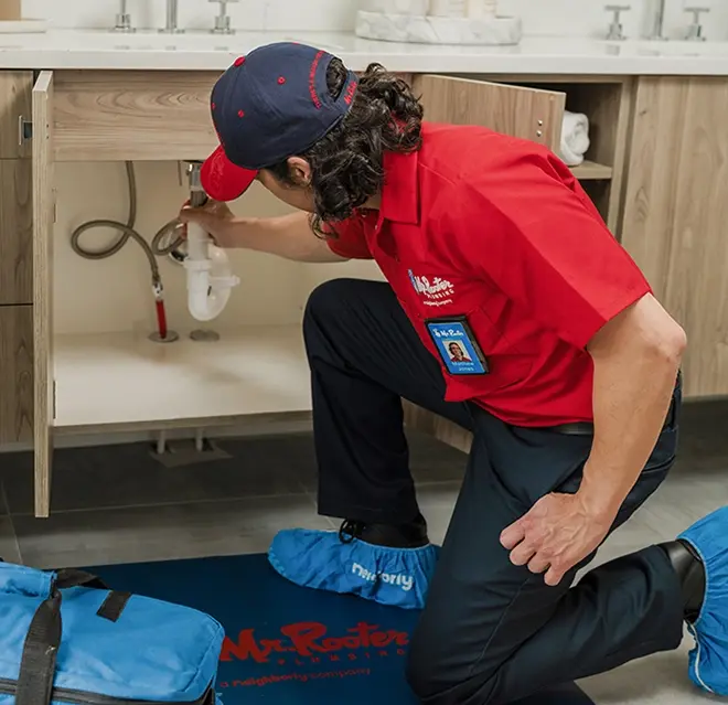 Mr. Rooter technician fixing a pipe under a sink vanity.