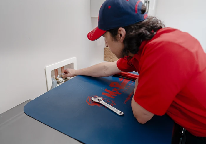 Mr. Rooter plumber doing drain repair work in a laundry room 