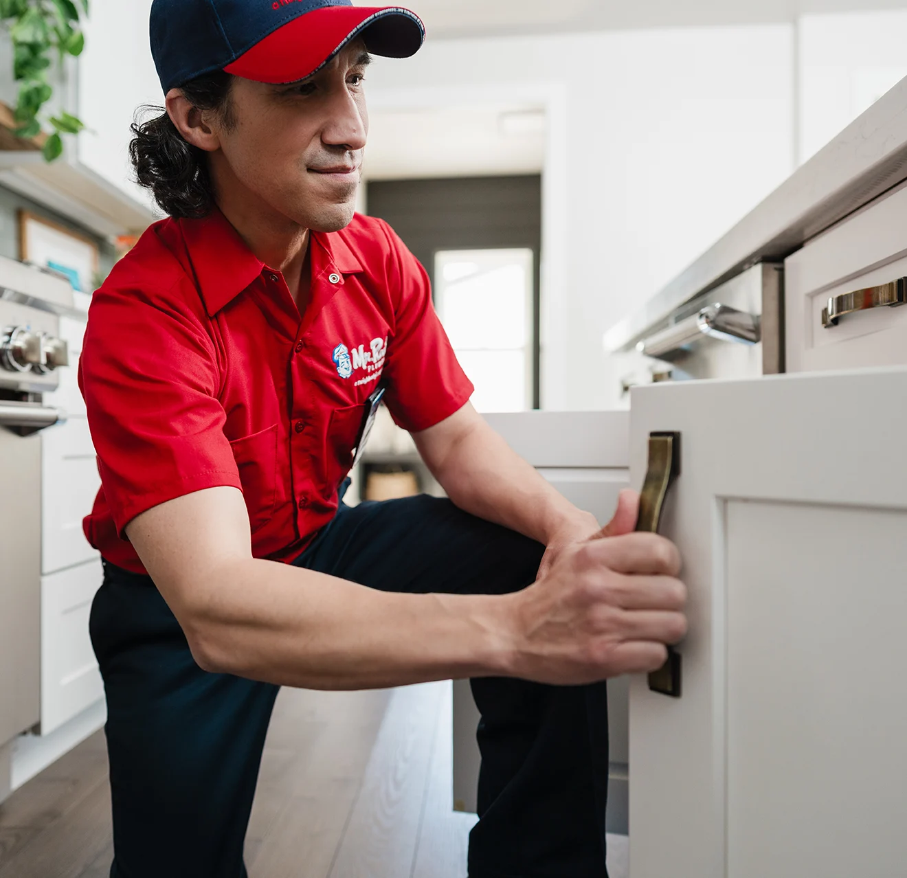 Mr. Rooter technician opening lower cabinet doors.