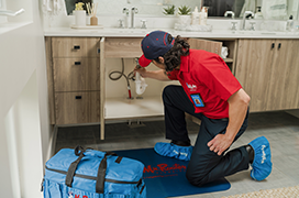 Mr. Rooter Plumbing technician cleaning under a sink vanity.