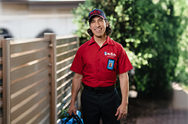 Mr. Rooter professional standing outside by a fence with greenery in the background.