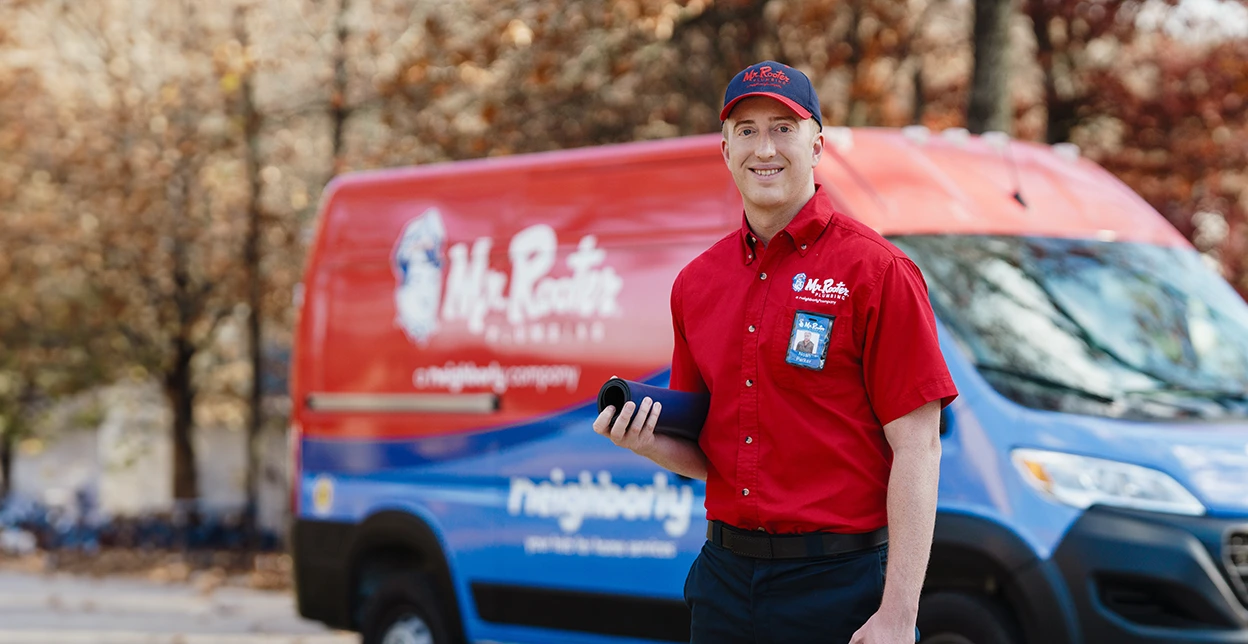 Smiling Mr. Rooter technician standing beside a branded van.