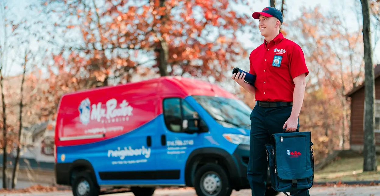 Mr. Rooter technician walking up to a customer's home with branded van in the background.