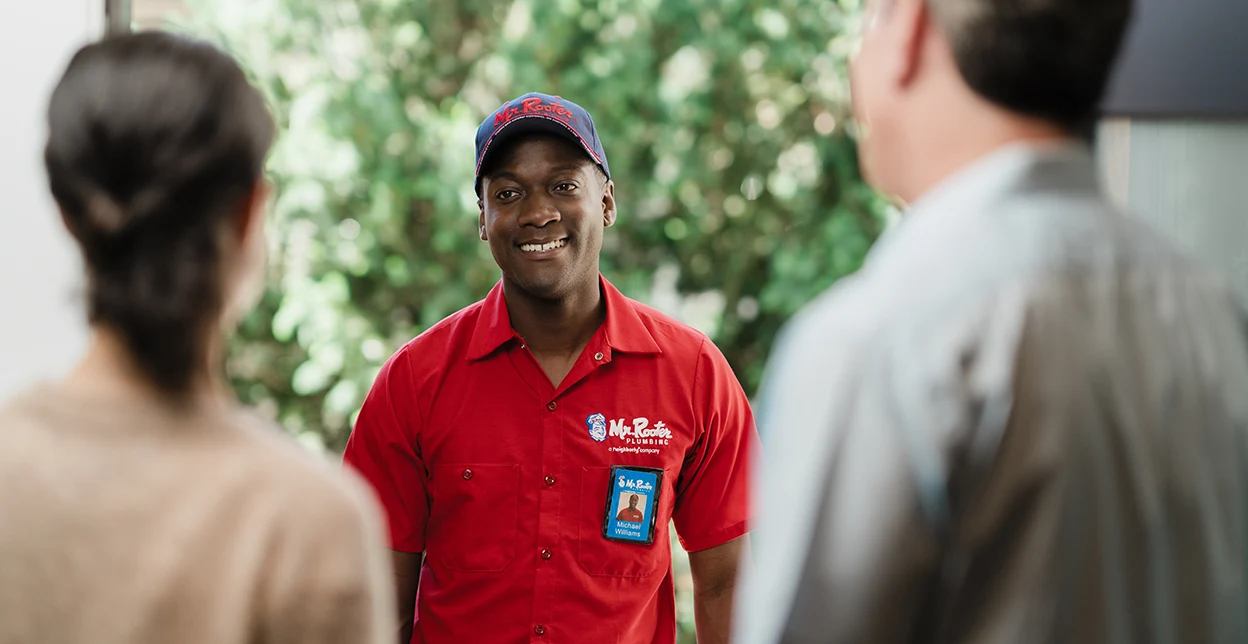 Two customers greeting a Mr. Rooter technician at their front door.