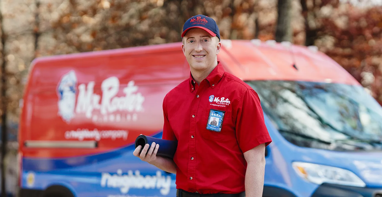 Mr. Rooter technician standing in front of a branded work van.