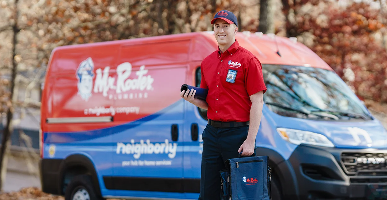 Mr. Rooter professional standing in front of a branded work van.