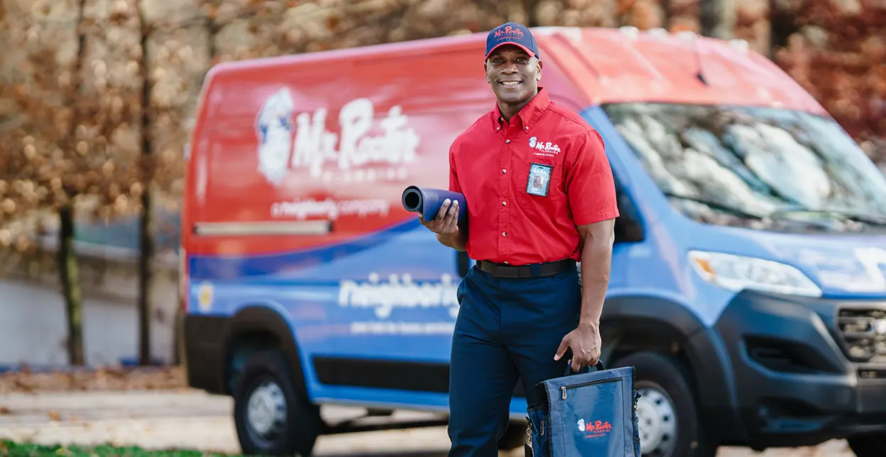 Mr. Rooter technician standing in front of a branded work van.