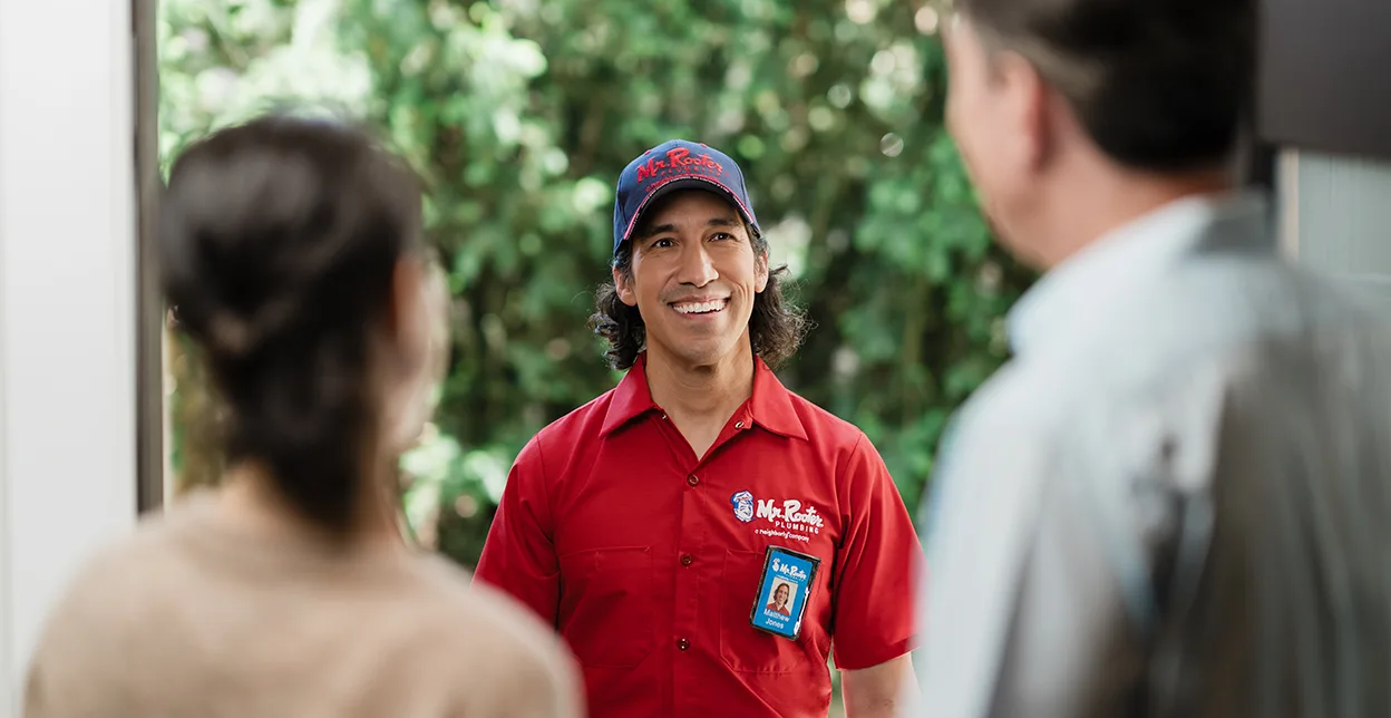 Smiling Mr. Rooter technician being greeted at a customer's door.