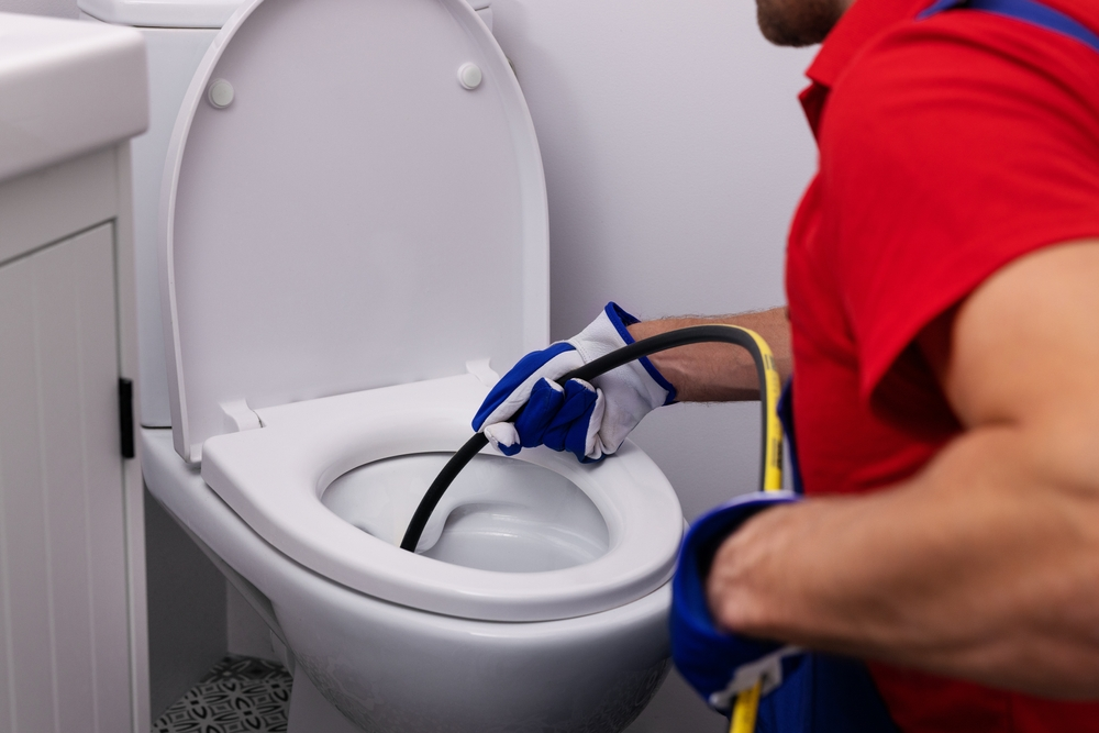 plumber unclogging blocked toilet with hydro jetting at home bathroom.