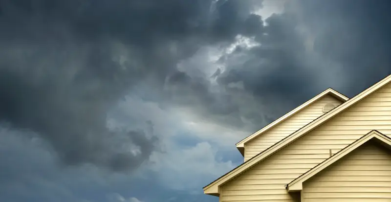Exterior of a residential home under dark storm clouds, representing hurricane preparation and plumbing safety planning before severe weather.