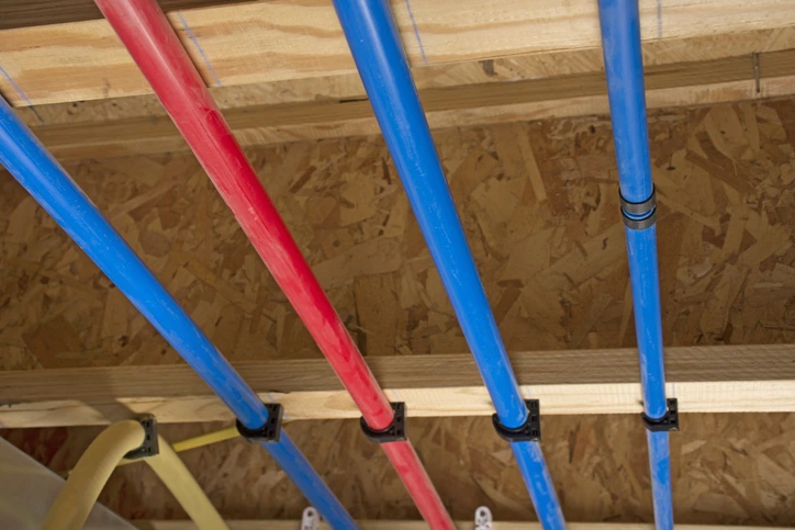 A group of four PEX pipes, three blue and one red, fixed to wood framing. | Mr. Rooter® Plumbing of Southeast Georgia