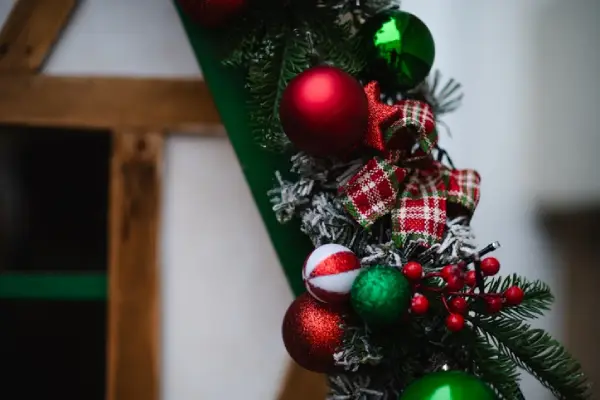 A detailed view of a Christmas garland decorated with red and white ornaments, plaid ribbons, pinecones, and berries