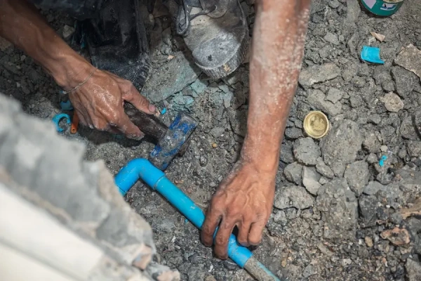 A plumber’s hands installing a PVC pipe in a concrete floor.