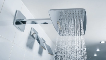 Water coming from a square shower head in modern bathroom with white tile.