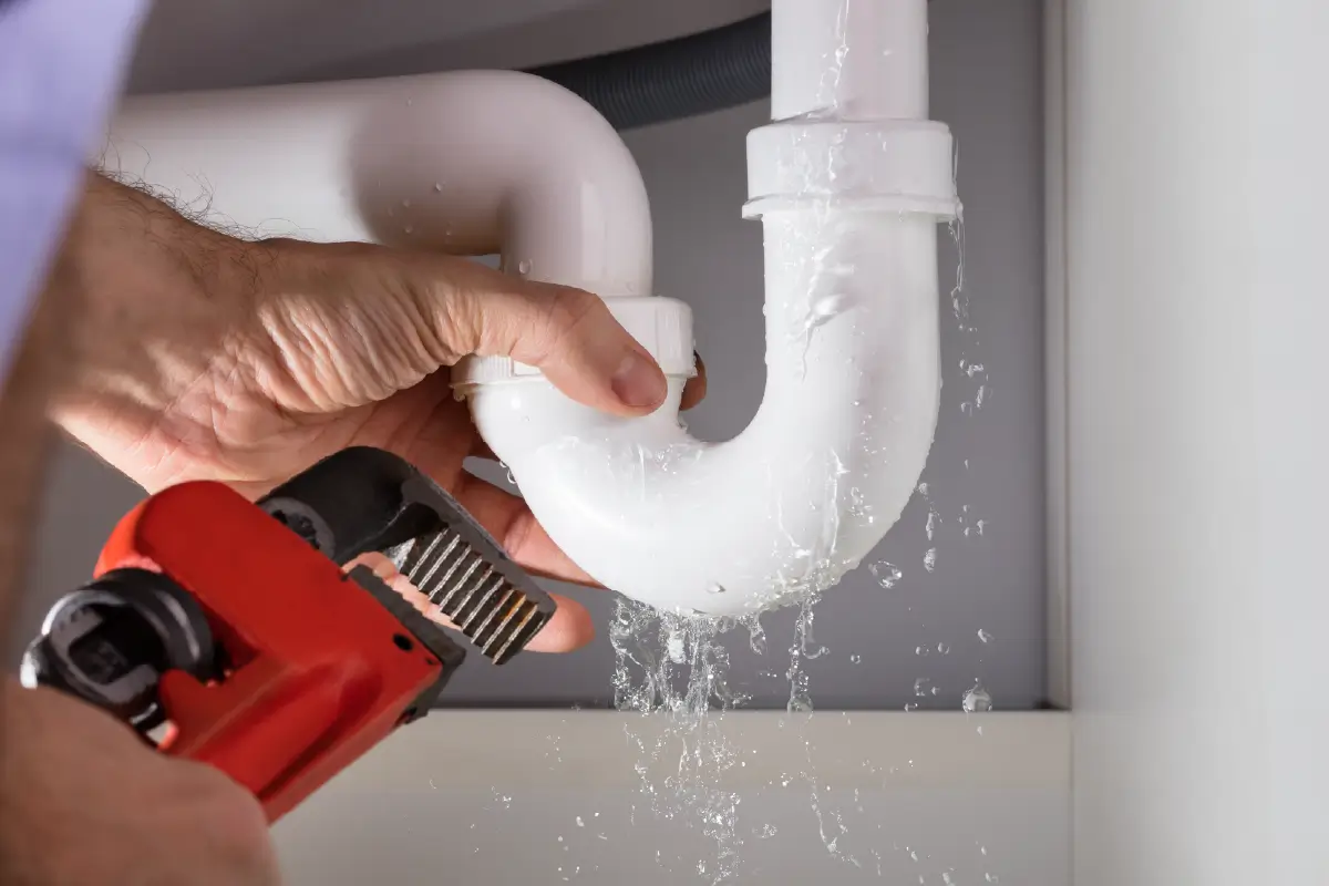 A person fixing a leaking pipe underneath a sink.