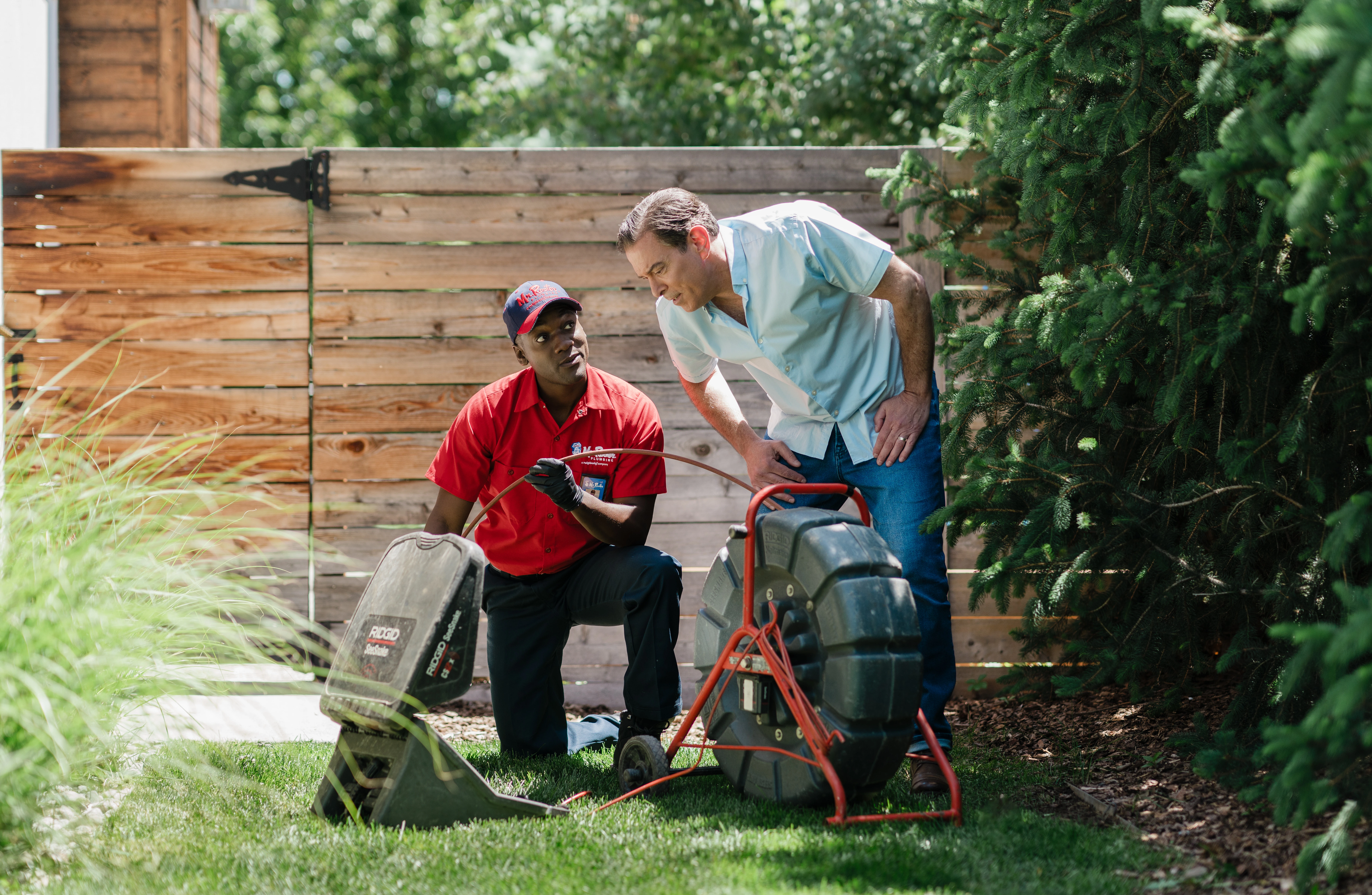 A Mr. Rooter service professional showing a homeowner how to use video camera inspection equipment to locate tree roots in a sewer line.